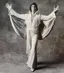 Elvis impersonator in white rhinestone jumpsuit with cape spread wide against gray textured backdrop, demonstrating versatile neutral backdrop for entertainment and performance photography